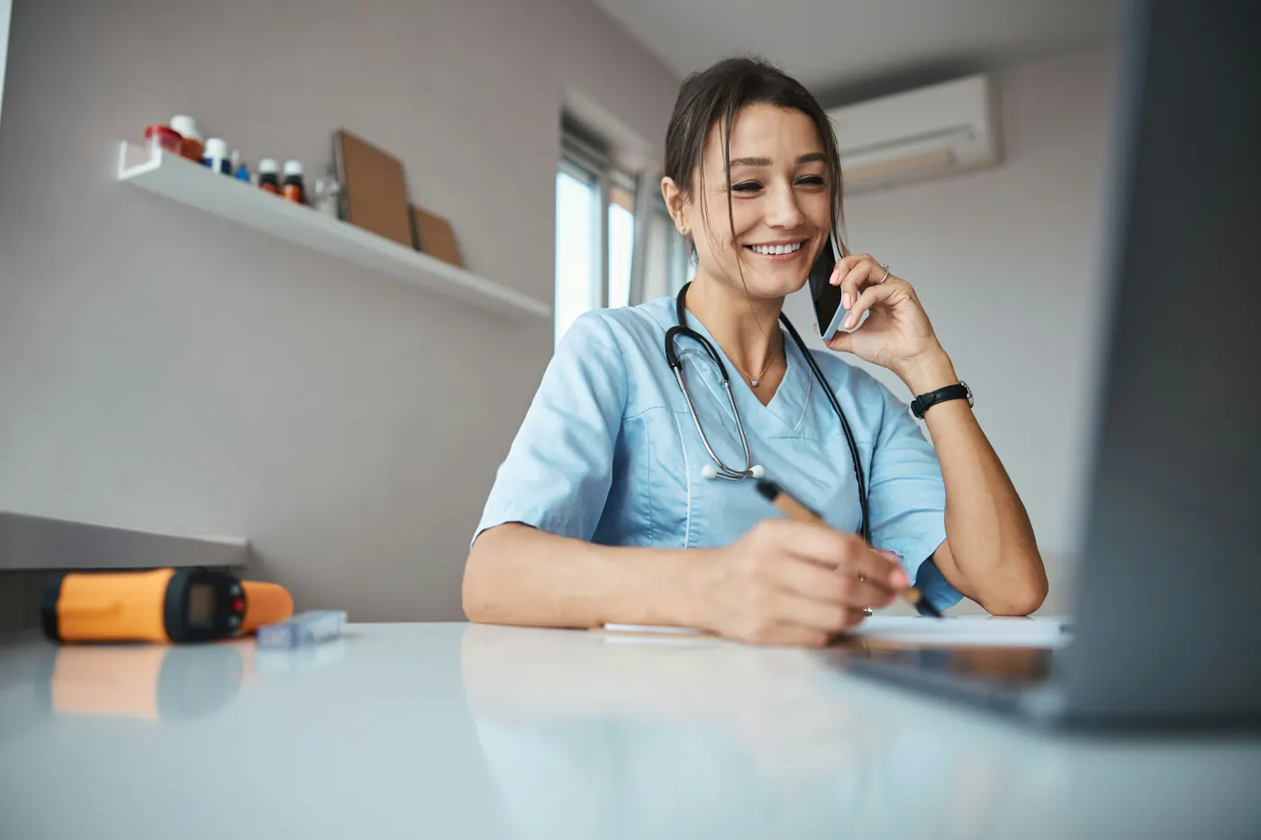 A smiling veterinary team member in scrubs taking a call at the clinic desk